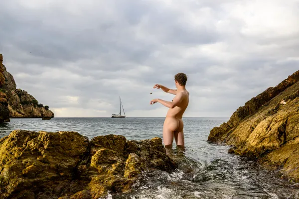 Fine art photography artwork named SIREN 1/3 of a solitary man in the ocean, throwing a stone to a sailboat by Arjan Spannenburg, exploring the Siren myth.