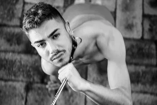 Black and white fine art carpet print of COMPELLED - DAMIAN by Arjan Spannenburg, featuring a man with a collar and chain.