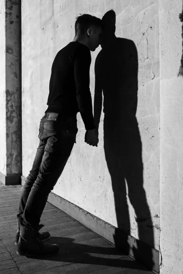 A minimalist black and white study of a man finding support within himself while leaning against a textured wall on an abandoned theater stage, exploring themes of self-reliance and the internal architecture of the human spirit.