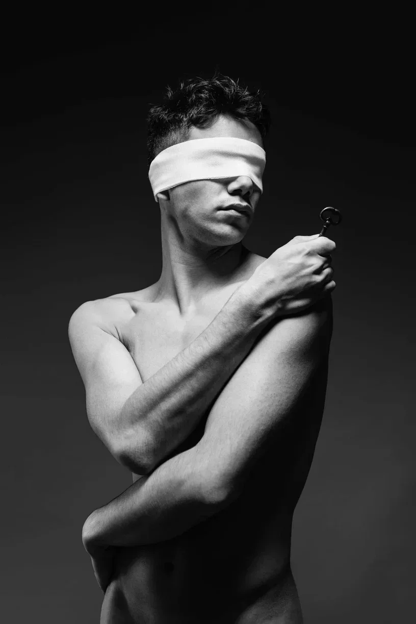 Schwarz-Weiß-Fotografie eines Mannes mit verbundenen Augen, der einen Skelettschlüssel hält, ein Symbol für inneres Vertrauen und verborgene Kraft.