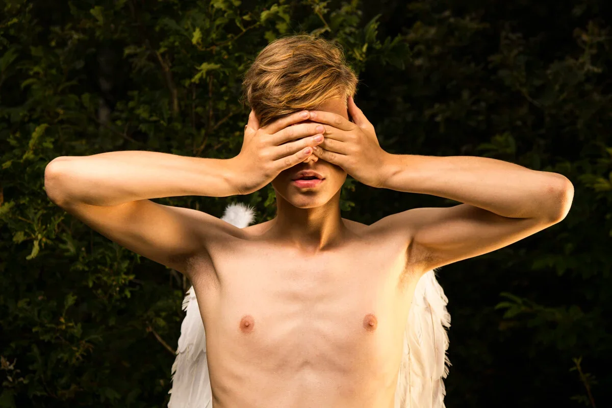 Ein geflügelter Mann bedeckt seine Augen mit den Händen vor einem dunklen Waldhintergrund, was ein Gefühl der inneren Reflexion hervorruft.