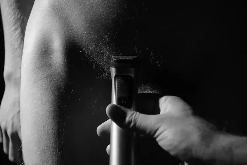 Monochrome study: A hand holding an electric razor shaves body hair. Close-up, intimate.