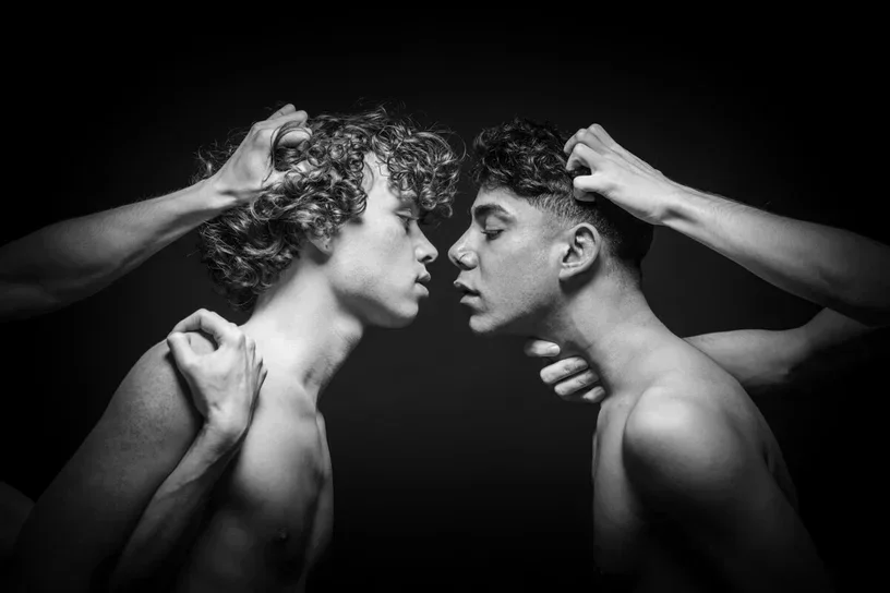 Schwarz-Weiß-Fotokunst mit dem Titel Restraint 3, die zwei Männer zeigt, die von äußeren Händen in einem dunklen Raum kontrolliert werden.