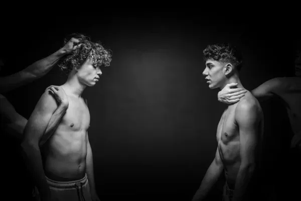 Black and white fine art photography titled Restraint I showing two men controlled by external hands in a dark space.