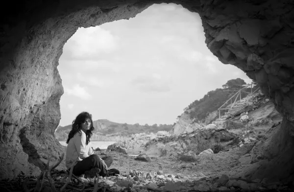 Black and white fine art photograph of a figure sitting inside a coastal cave overlooking a Mediterranean landscape.